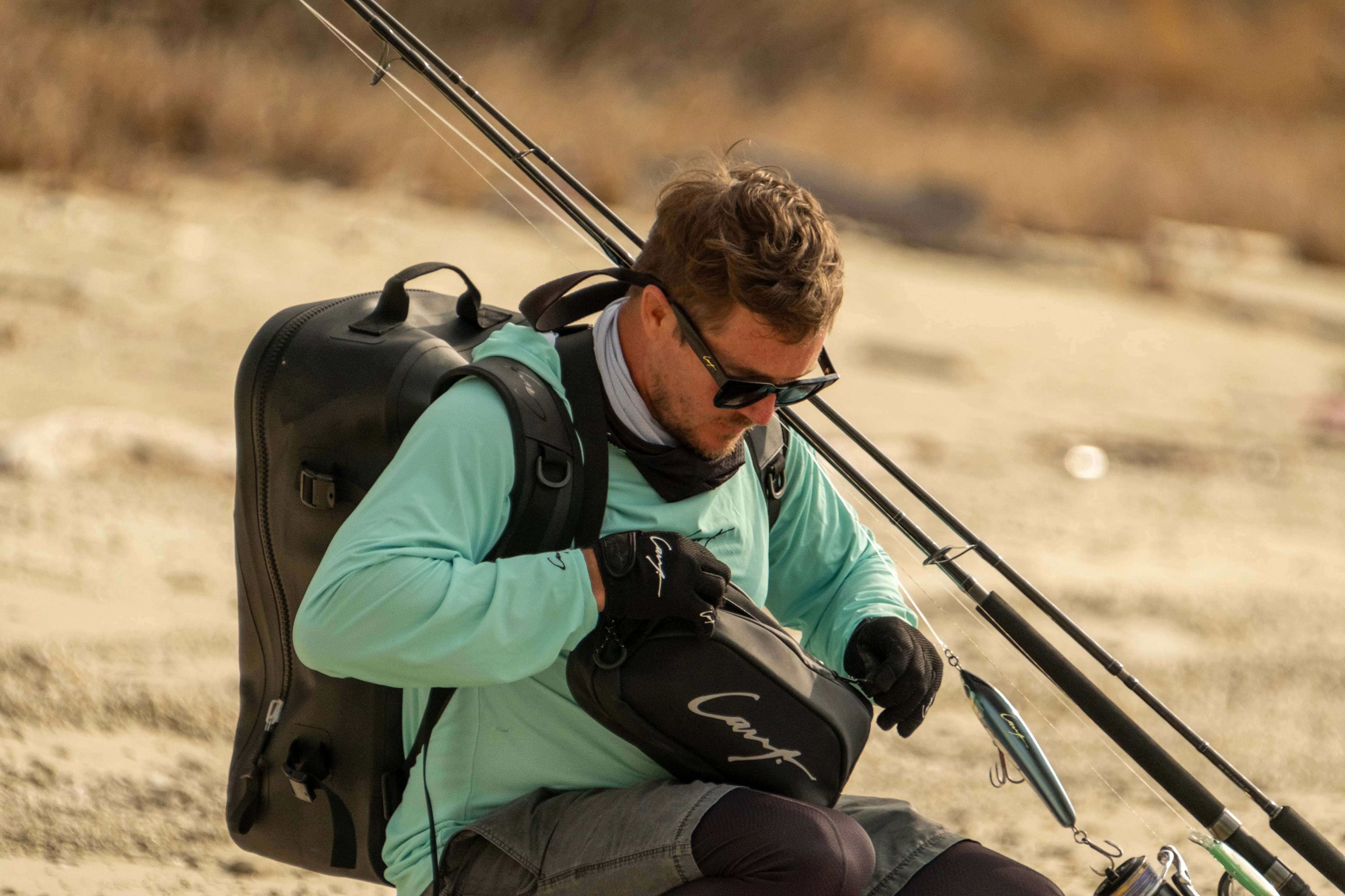 Angler preparing saltwater fishing gear with Cavy tackle storage bag, rods, and lures on the beach.