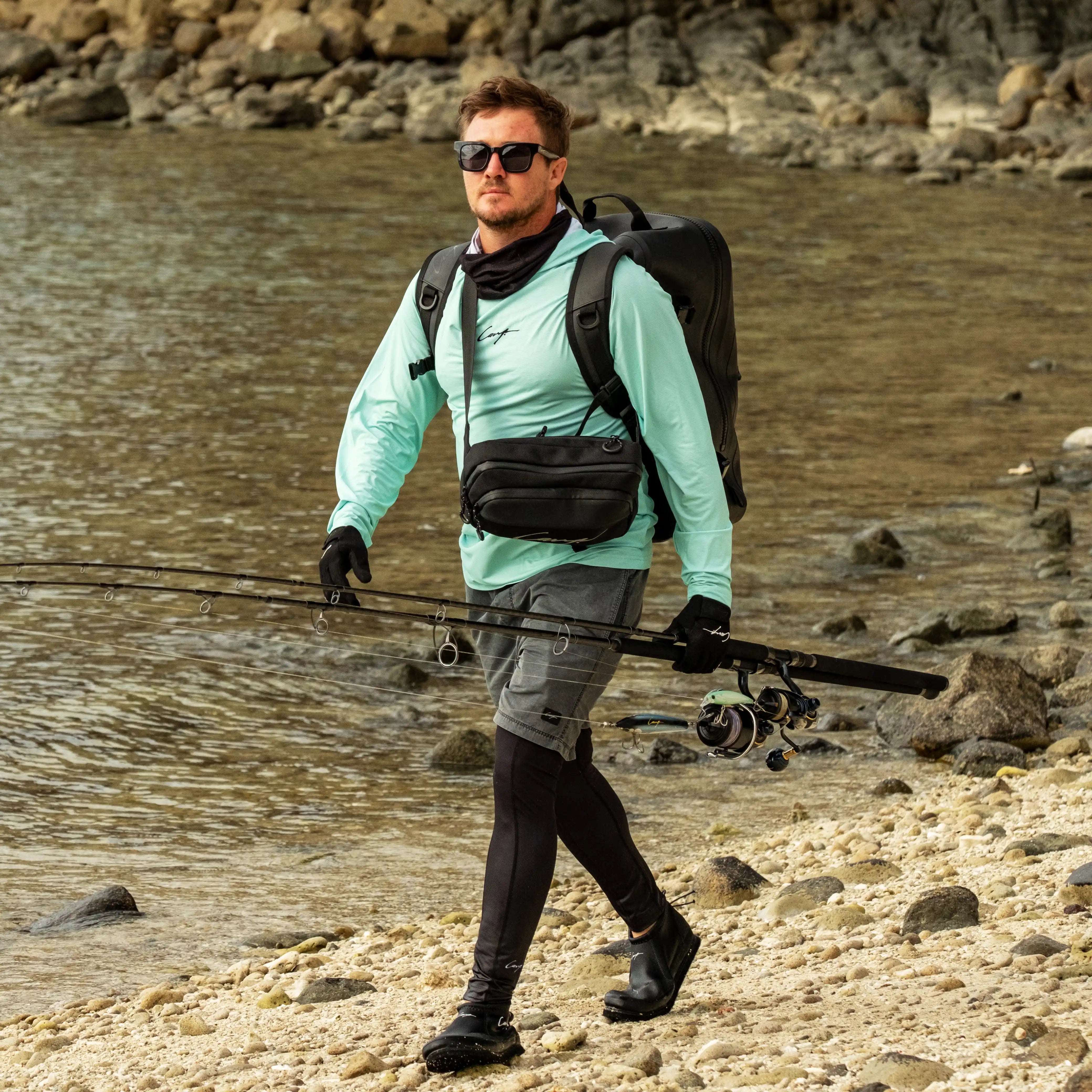 Man with fishing gear walking along a rocky shoreline