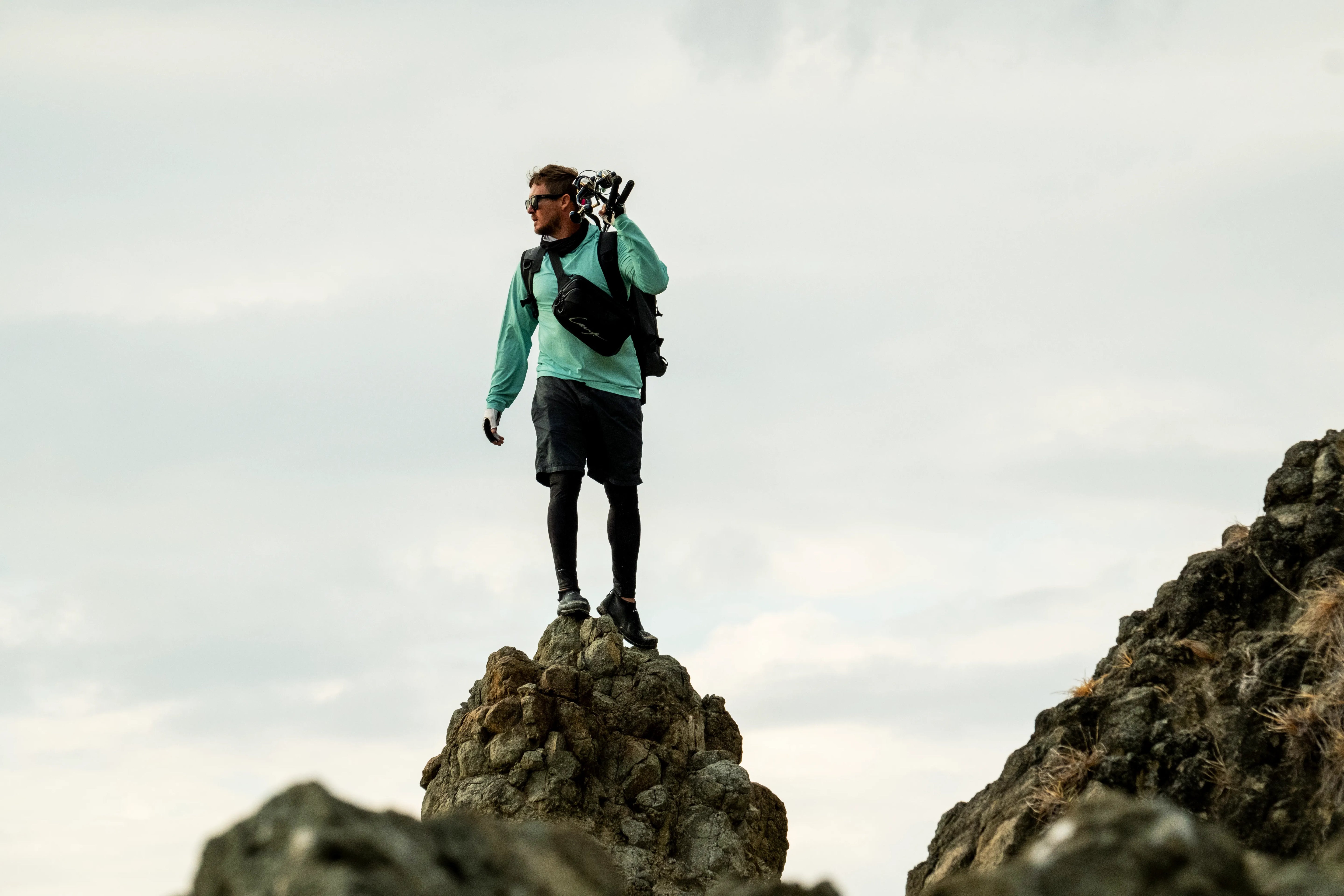 Adam Cavanagh wearing gear bags, stands on the rocks