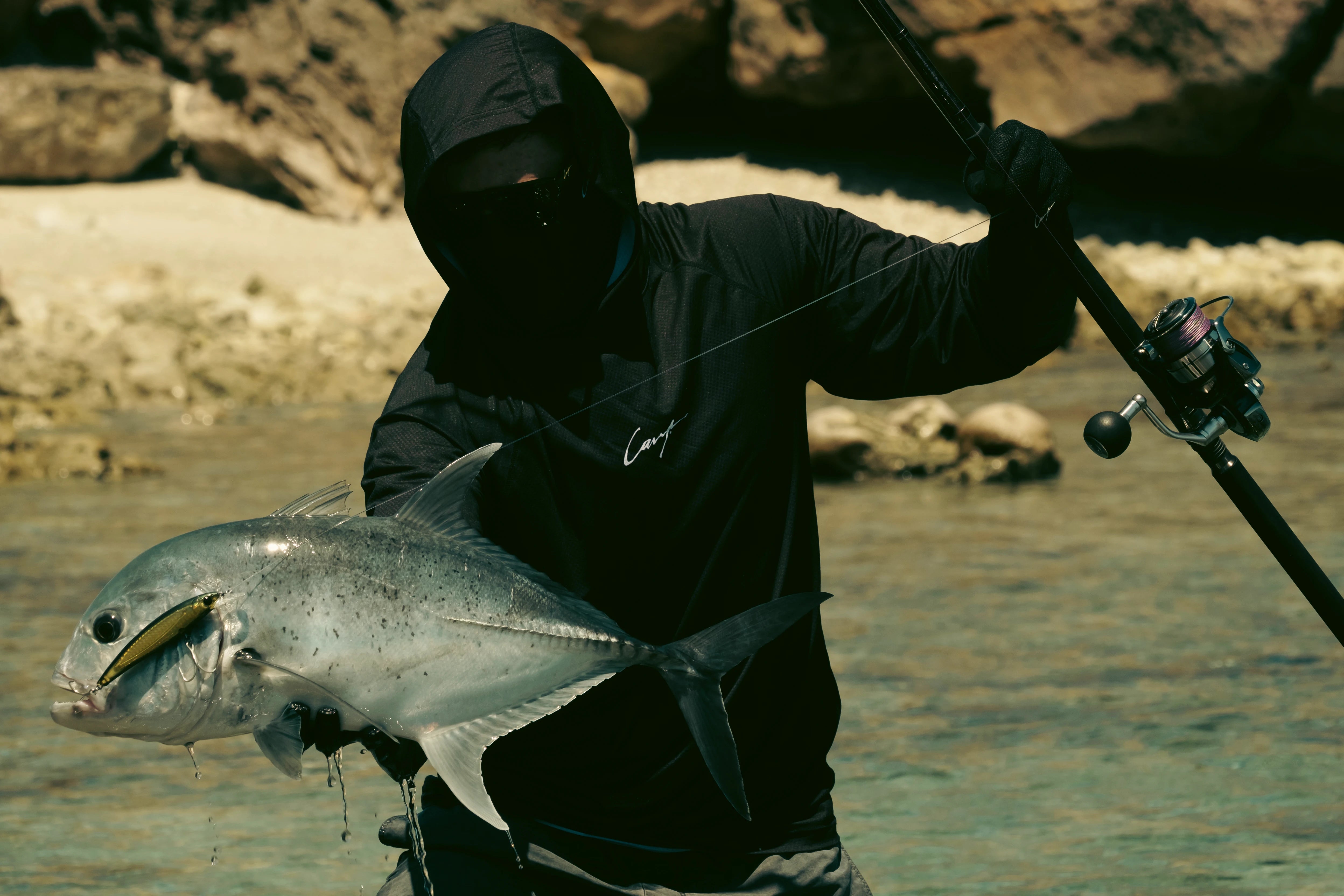 Fisherman wearing Cavy Fishing UV shirt and gloves fighting a giant trevally from the shoreline