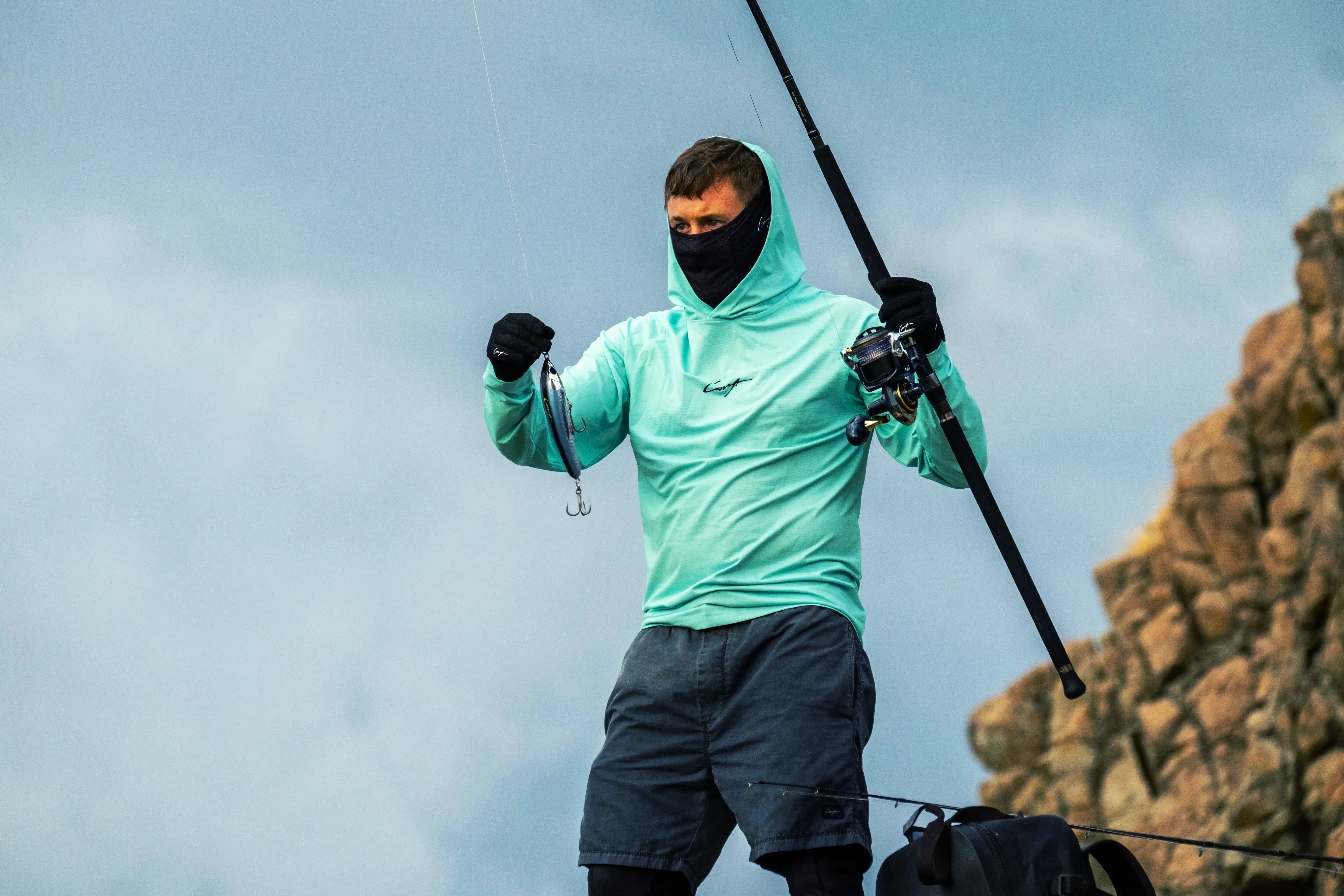Fishing apparel — angler wearing UV shirt, shorts, and Rock Hopper shoes while casting from rocky shore